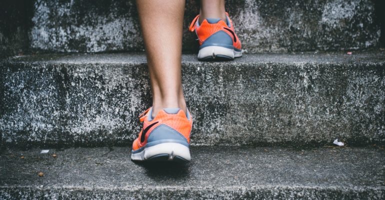 person wearing orange and gray Nike shoes walking on gray concrete stairs