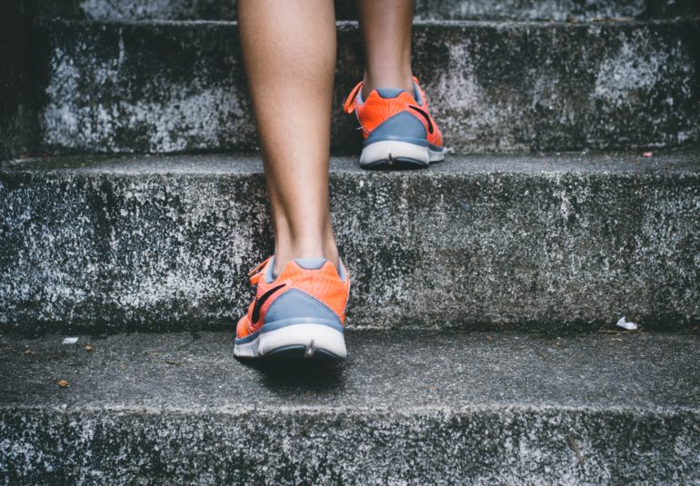 person wearing orange and gray Nike shoes walking on gray concrete stairs